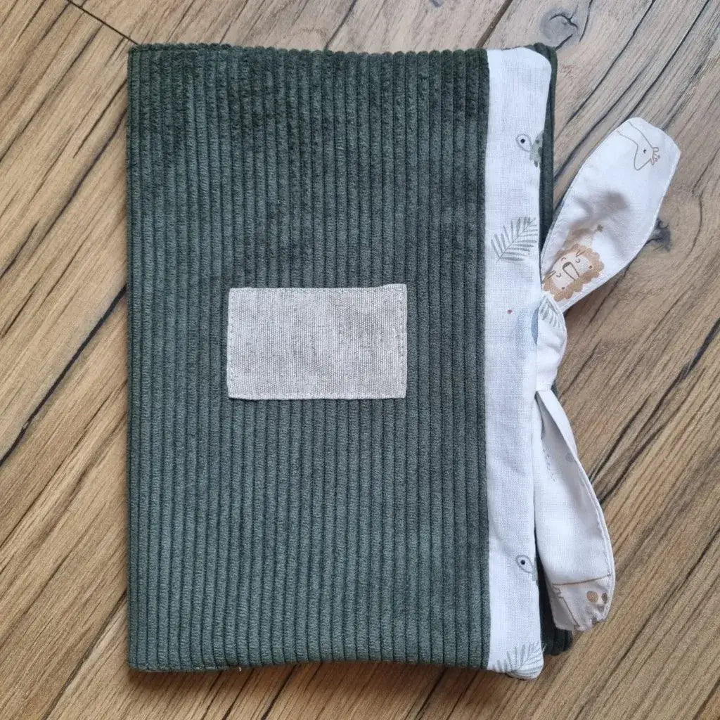 Protège carnet de santé en velours côtelé de coloris vert. Ce protège carnet de santé se ferme à l'aide d'un ruban en tissu imprimé au motif savane. Il est personnalisable avec le prénom de l'enfant floqué sur une petite étiquette en tissu.