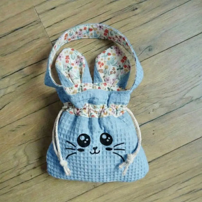 Sac pochon bleu en nid d'abeille avec flocage Chatoune noir et doublure fleurie colorée, posé sur un parquet.