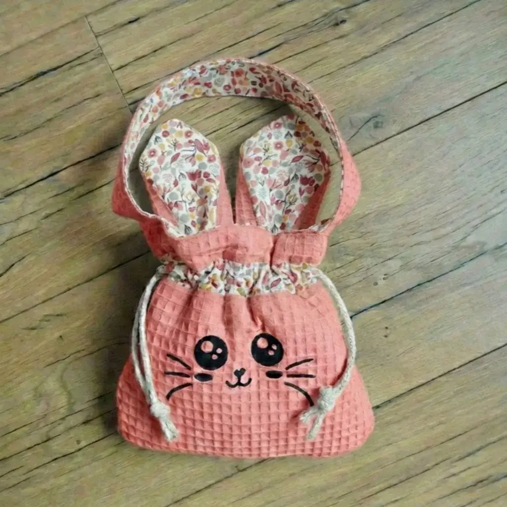 Sac pochon rose marsala en nid d'abeille avec visage Chatoune, anse et oreilles à fleurs, sur parquet.