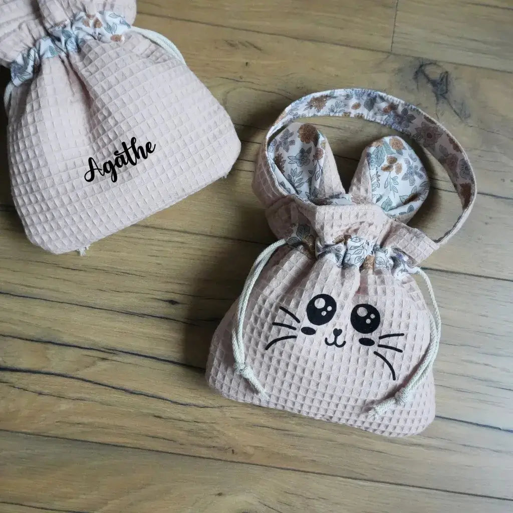 Deux pochons en nid d'abeille peau sur parquet : l'un avec le visage Chatoune, l'autre personnalisé au prénom Agathe.