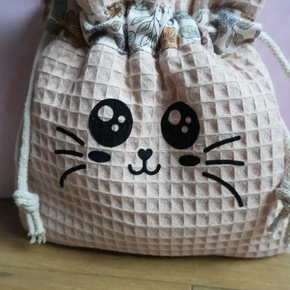 Zoom sur un pochon couleur peau en nid d'abeille avec le flocage Chatoune noir aux grands yeux expressifs et nez en cœur.