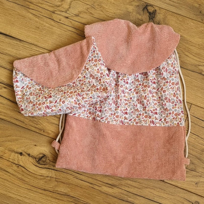 Sac à dos format pochon avec une base et un rabat en velours côtelé rose. Le corps du sac est composé d'un tissu au motif liberty. A gauche de ce sac est disposée une pochette assortie avec le même tissu motif liberty et un rabat en velours côtelé rose.