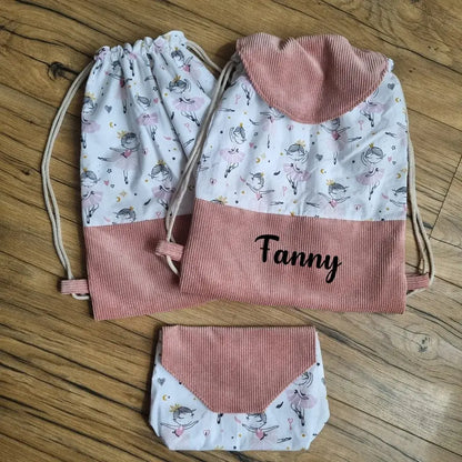 Ensemble cousu main composé d’un sac à dos pochon personnalisé avec le prénom "Fanny", d’un sac assorti et d’une pochette, confectionnés en velours côtelé rose et tissu blanc imprimé de petites danseuses. Idéal pour la danse ou l’école, cet ensemble unique allie praticité, douceur et style enfantin sur un fond en bois naturel.