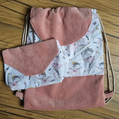 Ensemble assorti cousu main composé d’un sac à dos pochon et d’une pochette, en velours côtelé rose et tissu imprimé de petites danseuses. Le sac à cordon possède un rabat arrondi, et la pochette un rabat en triangle. Idéal pour la danse, l’école ou les sorties, cet ensemble pratique et esthétique est présenté sur un fond en bois naturel.