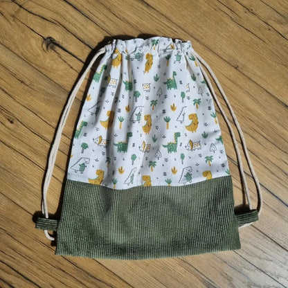 Sac à dos pochon pour enfant sans rabat, réalisé à la main avec tissu à motifs dinosaures colorés et base en velours côtelé vert kaki. Fermeture par cordons beiges pour un port facile sur le dos. Idéal pour la crèche, la maternelle ou les sorties. Accessoire léger, pratique et original, parfait pour les petits fans de dinosaures. Fabrication artisanale soignée.