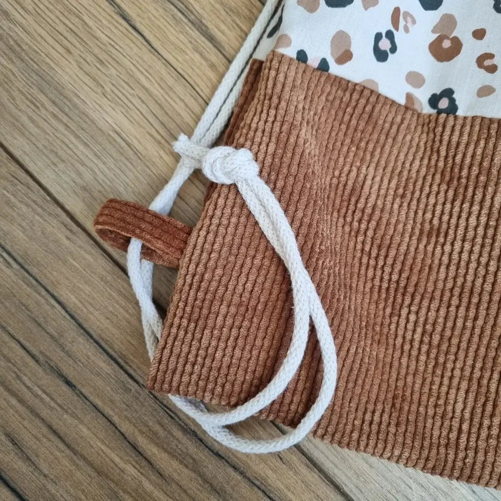 Détail de la base en velours côtelé marron du sac à dos pochon au motif léopard. On voit bien également la cordelette en coton blanc permettant la fermeture du sac.