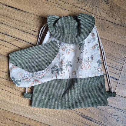 Sac à dos pochon pour enfant en tissu motif jungle avec rabat en velours côtelé vert, accompagné d’une pochette assortie. Ensemble fait main idéal pour la maternelle, les sorties ou comme cadeau personnalisé. Motifs animaux exotiques et palmiers sur fond clair.