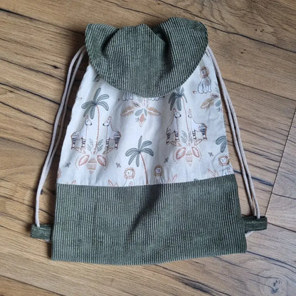 Sac à dos pochon fait main pour enfant, en tissu imprimé motif jungle avec animaux et palmiers, et base en velours côtelé vert. Fermeture par cordons coulissants et rabat arrondi assorti. Parfait pour la crèche, la maternelle ou comme cadeau personnalisé original.