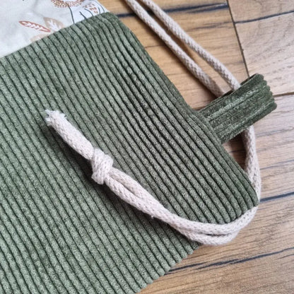 Zoom sur la base en velours côtelé vert d’un sac à dos pochon pour enfant, avec détail de la cordelette de fermeture écrue nouée. Fabrication artisanale avec finitions soignées. Tissu solide et esthétique, idéal pour un usage quotidien à l’école ou en sortie.