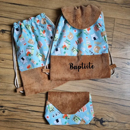 Ensemble cousu main comprenant un sac à dos personnalisé avec le prénom "Baptiste", un pochon et une pochette assortie, confectionnés en velours côtelé marron et tissu bleu à motifs kawaii (nourriture japonaise, animaux mignons). Accessoires enfant originaux et personnalisables, parfaits pour l’école, la crèche ou les sorties.