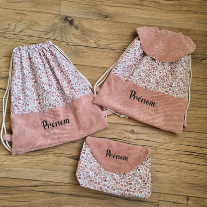 Ensemble sacs à dos format pochon motif liberty personnalisés au prénom. A gauche, un sac à dos format pochon avec une base en velours côtelé rose. Le corps du sac est composé d'un tissu au motif liberty. A droite, le même sac mais avec un rabat en velours côtelé rose. En bas, une pochette assortie avec le même tissu motif liberty et un rabat en velours côtelé rose.