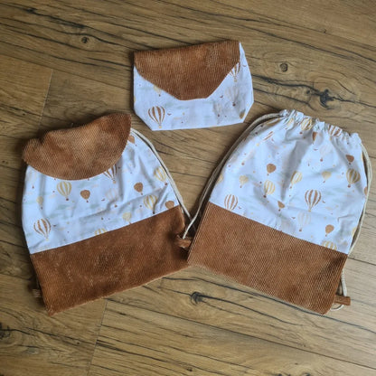 Ensemble assorti de deux sacs à dos pochons et d'une pochette imperméable au motif montgolfière. Le sac à dos de droite est sans rabat. Celui de gauche dispose d'un rabat en velours côtelé de couleur marron.