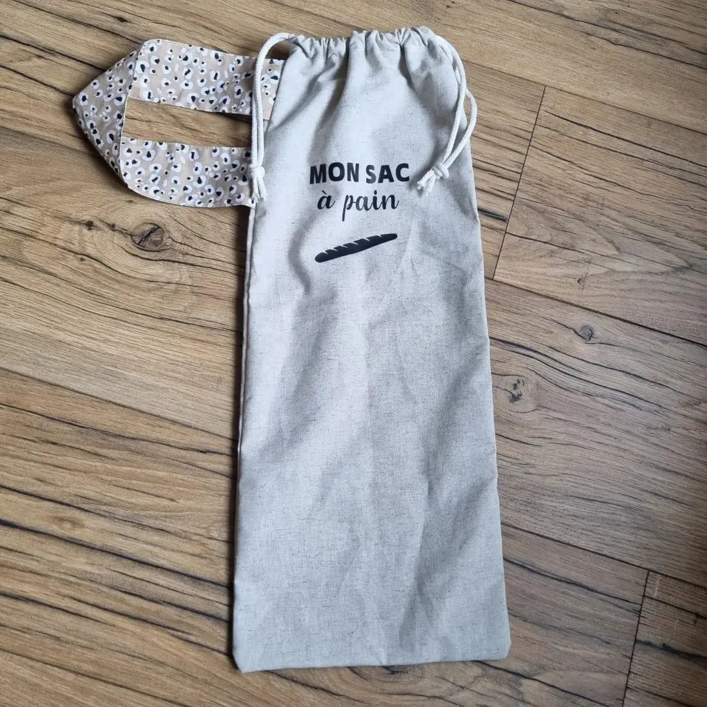 Sac à pain en coton au format baguette se fermant par deux petites cordelettes blanches avec une sangle au motif léopard et l'inscription "Mon sac à pain" et le logo d'une baguette floqués au centre sur la partie supérieure haute.