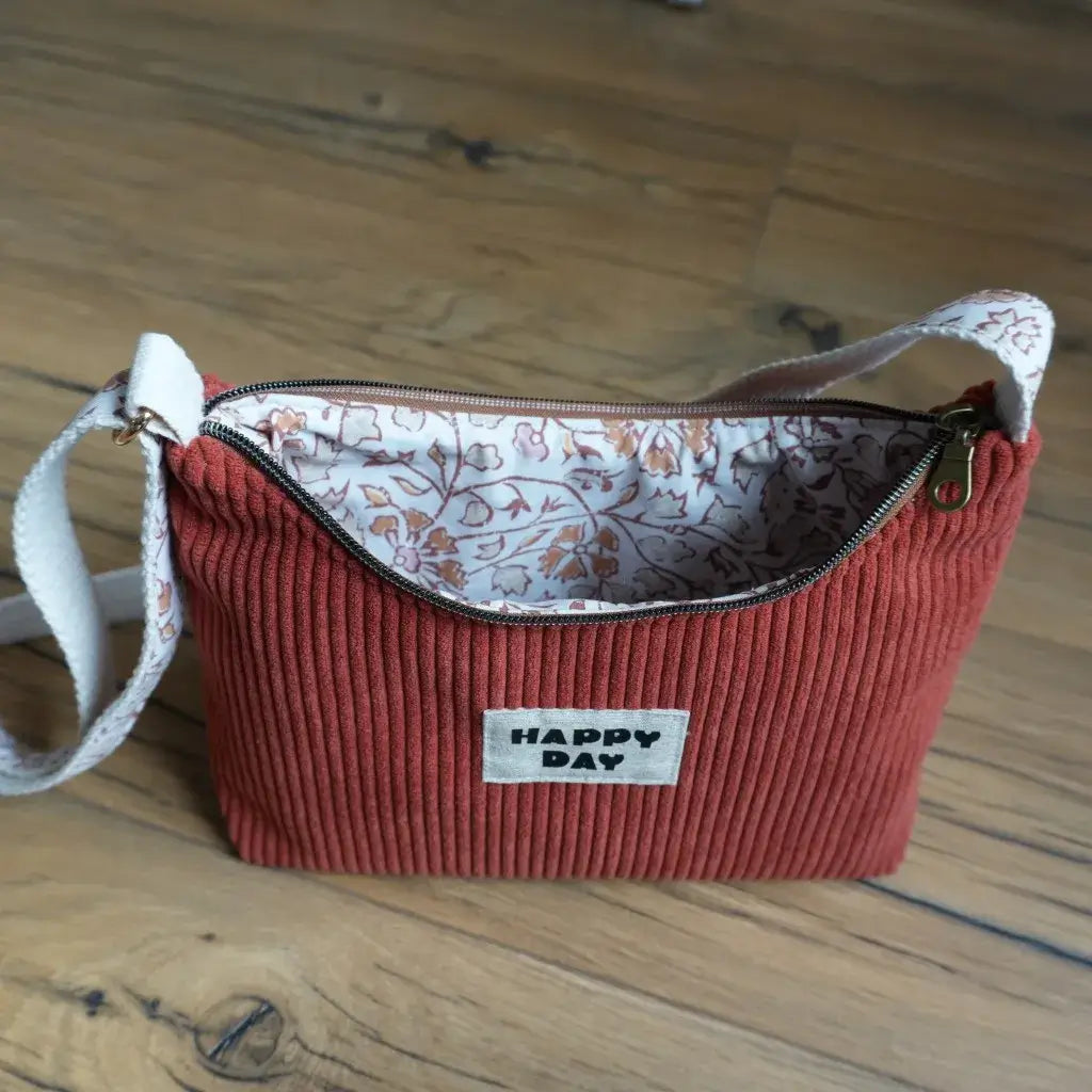 Sac bandoulière en velours côtelé terracotta avec doublure en coton fleuri oriental dans des tons beiges et rosés, équipé d’une fermeture éclair métallique et d’une sangle ajustable en coton écru. Accessoire mode artisanal et pratique, ce sac fait main allie élégance et originalité, parfait pour transporter ses affaires du quotidien avec style et ajouter une touche tendance et personnalisée à sa tenue.