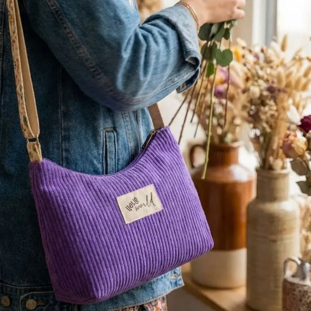 Sac bandoulière violet lavande en velours côtelé porté à l'épaule.
