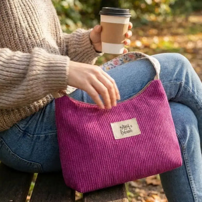 Sac bandoulière magenta en velours côtelé porté sur les genoux en extérieur.