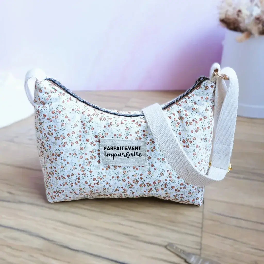Sac bandoulière en tissu blanc à petites fleurs liberty couleur rouille et beige, anse écrue et étiquette 'Parfaitement imparfaite'. Sac léger et romantique, idéal pour un style champêtre et féminin, parfait pour le quotidien ou les balades. Photo posée sur parquet clair avec décor épuré et touche de fleurs séchées en arrière-plan.