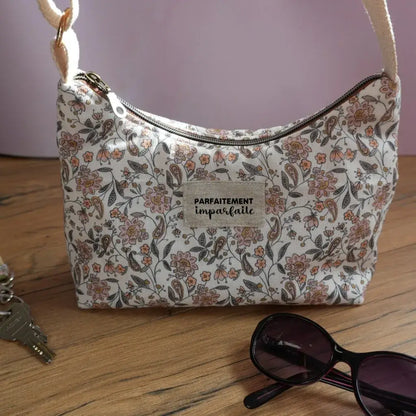 Sac bandoulière en tissu à motif fleuri délicat dans les tons rose poudré et brun, étiquette 'Parfaitement imparfaite' et anse écrue. Accessoire chic et féminin, parfait pour compléter un look romantique ou bohème. Photo sur parquet clair avec lunettes de soleil et trousseau de clés pour une ambiance estivale et élégante.
