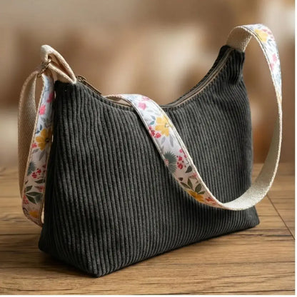 Sac bandoulière noir en velours côtelé avec sangle colorée à motifs floraux.
