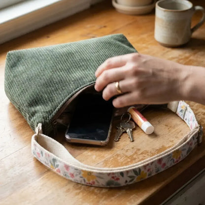 Sac bandoulière velours côtelé vert ouvert avec téléphone, clés et baume à lèvres.
