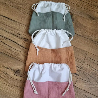 Trois pochons imperméables en tissu double gaze de coton uni disposés l'un au-dessus de l'autre. Celui du haut est de coloris kaki, celui du milieu de coloris camel et celui du bas est de coloris rose.