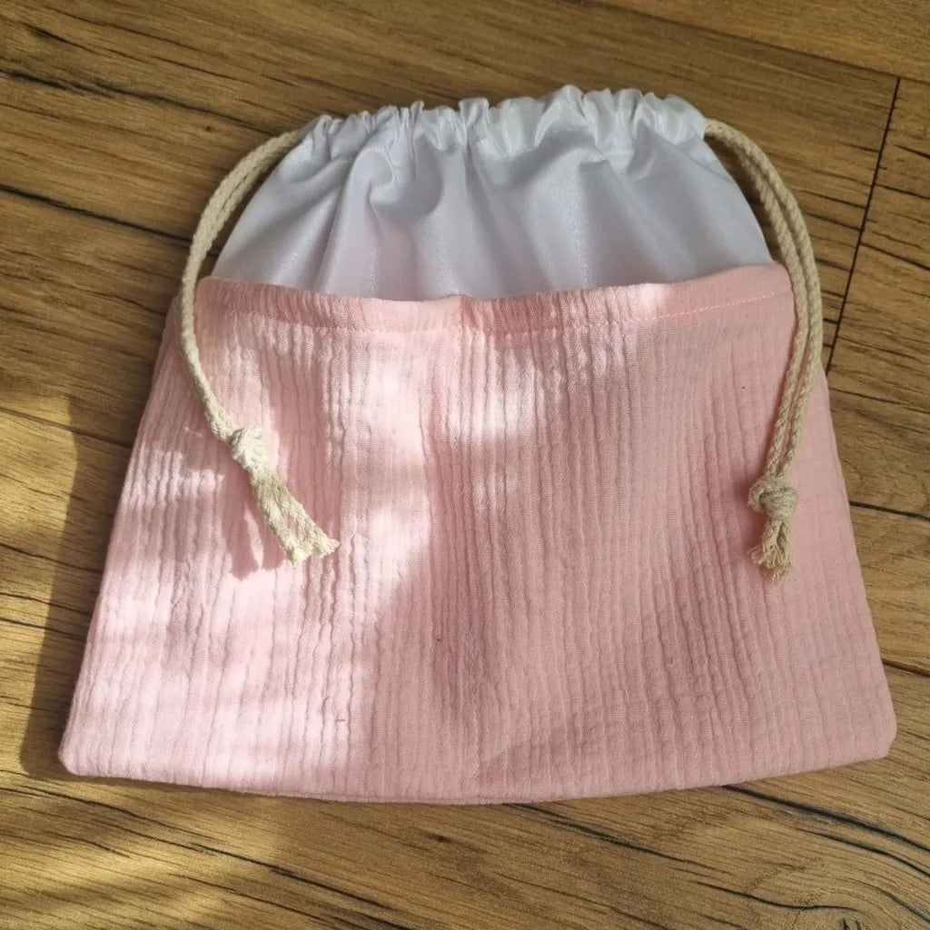 Sac piscine imperméable au format pochon se fermant grâce à deux cordelettes en coton blanc de part et d'autre et cousu avec un tissu en double gaze de coton uni de coloris rose pâle.