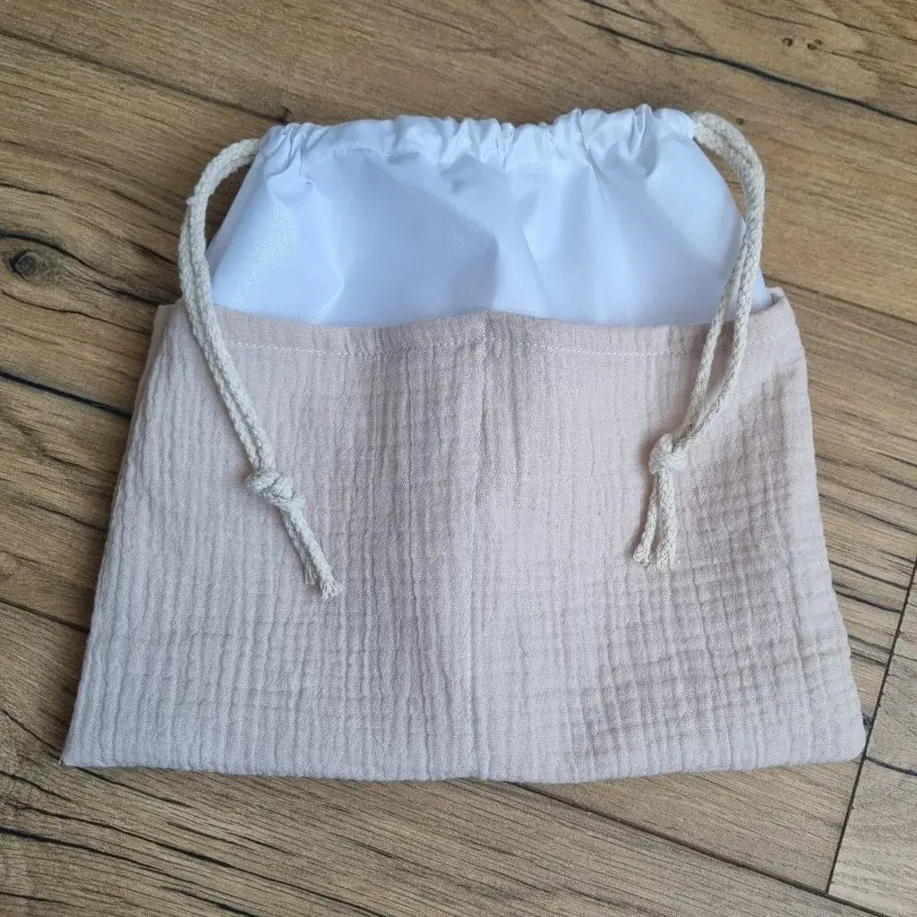 Sac piscine imperméable au format pochon se fermant grâce à deux cordelettes en coton blanc de part et d'autre et cousu avec un tissu en double gaze de coton uni de coloris sable.