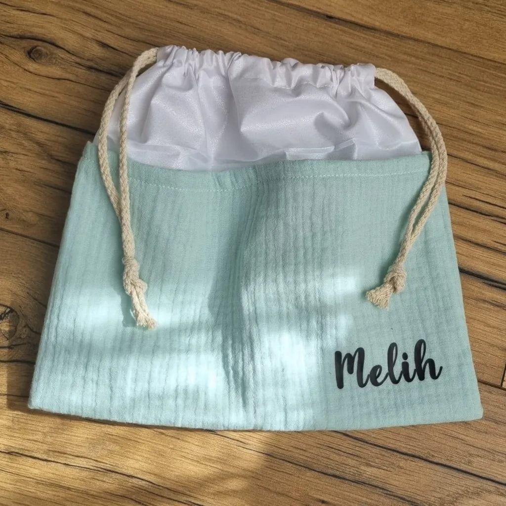 Sac piscine imperméable au format pochon se fermant grâce à deux cordelettes en coton blanc de part et d'autre et cousu avec un tissu en double gaze de coton uni de coloris vert menthe. Le sac pochon est personnalisé avec le prénom "Melih" floqué en bas à droite.