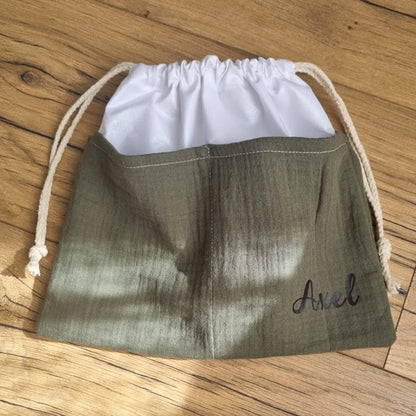 Sac piscine imperméable au format pochon se fermant grâce à deux cordelettes en coton blanc de part et d'autre et cousu avec un tissu en double gaze de coton uni de coloris vert. Le sac pochon est personnalisé avec le prénom "Axel" floqué en bas à droite.