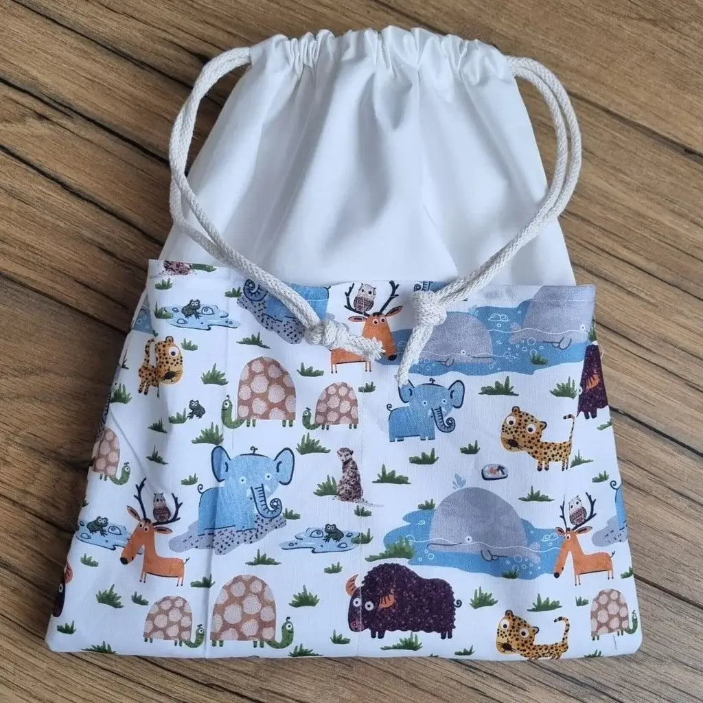 Sac piscine imperméable au format pochon se fermant grâce à deux cordelettes en coton blanc de part et d'autre et cousu avec un tissu imprimé à motif d'animaux comme des bisons, des éléphants, des baleines, des tortues ou des tigres.