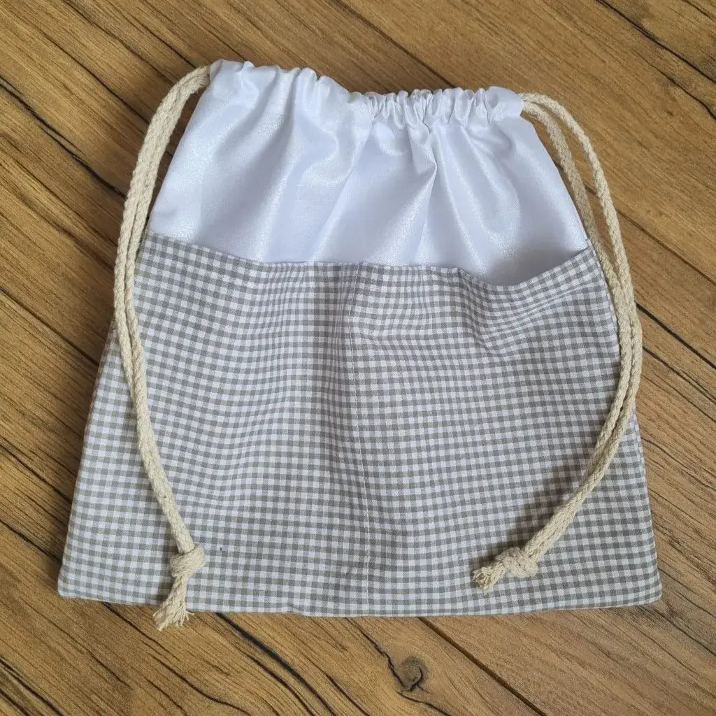 Sac piscine imperméable au format pochon se fermant grâce à deux cordelettes en coton blanc de part et d'autre et cousu avec un tissu imprimé à motif carreaux beiges.