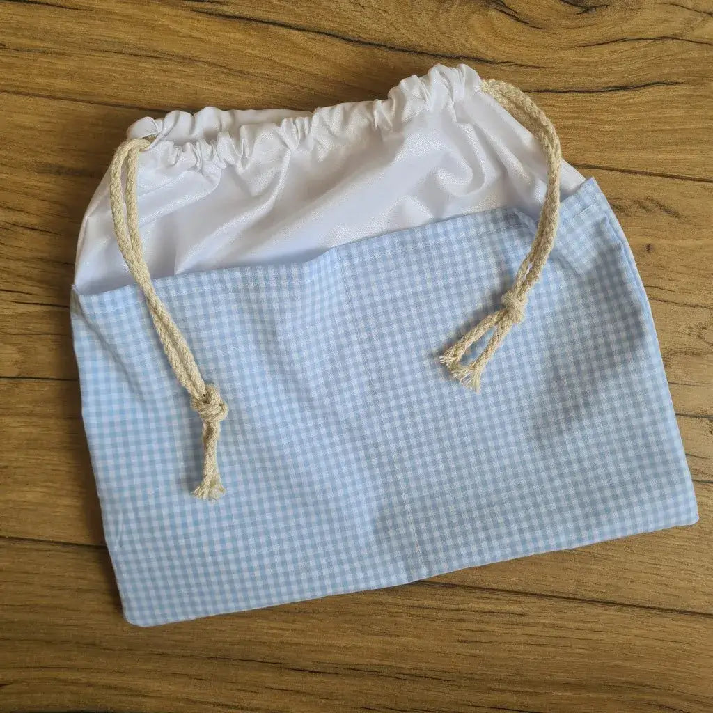 Sac piscine imperméable au format pochon se fermant grâce à deux cordelettes en coton blanc de part et d'autre et cousu avec un tissu imprimé à motif carreaux bleus.