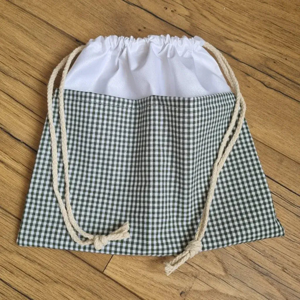 Sac piscine imperméable au format pochon se fermant grâce à deux cordelettes en coton blanc de part et d'autre et cousu avec un tissu imprimé à motif carreaux verts.