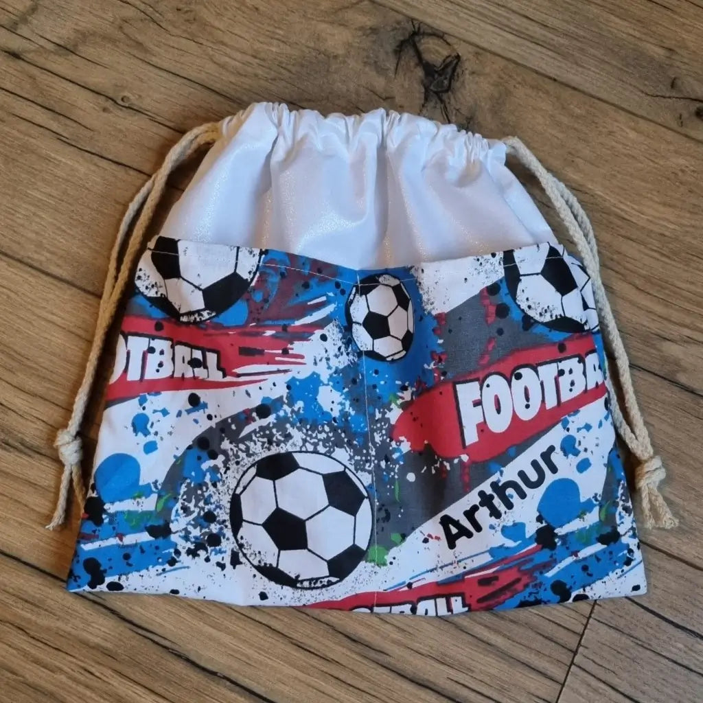 Sac piscine imperméable au format pochon se fermant grâce à deux cordelettes en coton blanc de part et d'autre et cousu avec un tissu imprimé à motif football avec une dominante de bleu.