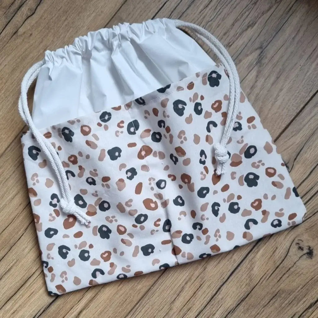 Sac piscine imperméable au format pochon se fermant grâce à deux cordelettes en coton blanc de part et d'autre et cousu avec un tissu imprimé à motif léopard.