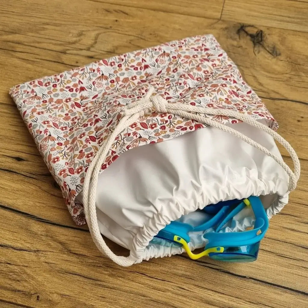 Sac piscine imperméable au format pochon se fermant grâce à deux cordelettes en coton blanc de part et d'autre et cousu avec un tissu imprimé à motif liberty.