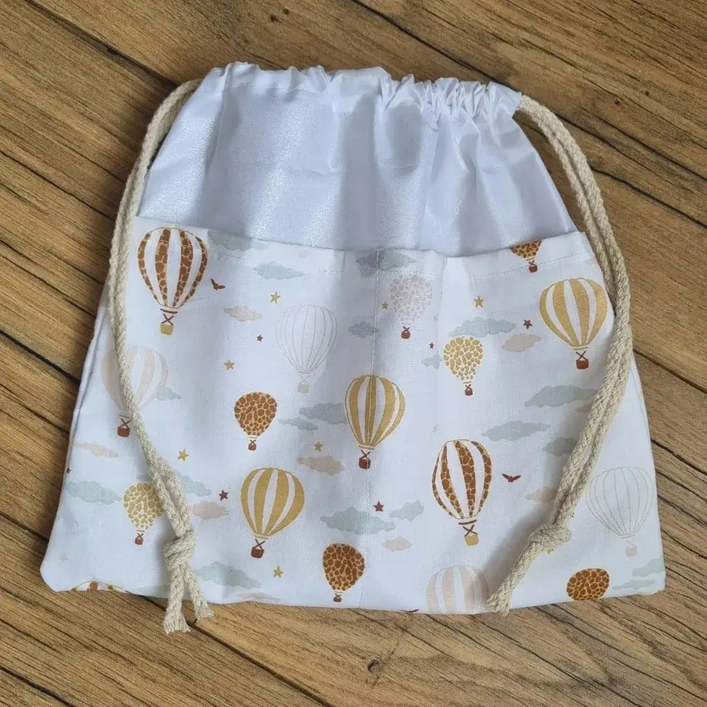 Sac piscine imperméable au format pochon se fermant grâce à deux cordelettes en coton blanc de part et d'autre et cousu avec un tissu imprimé à motif montgolfières.