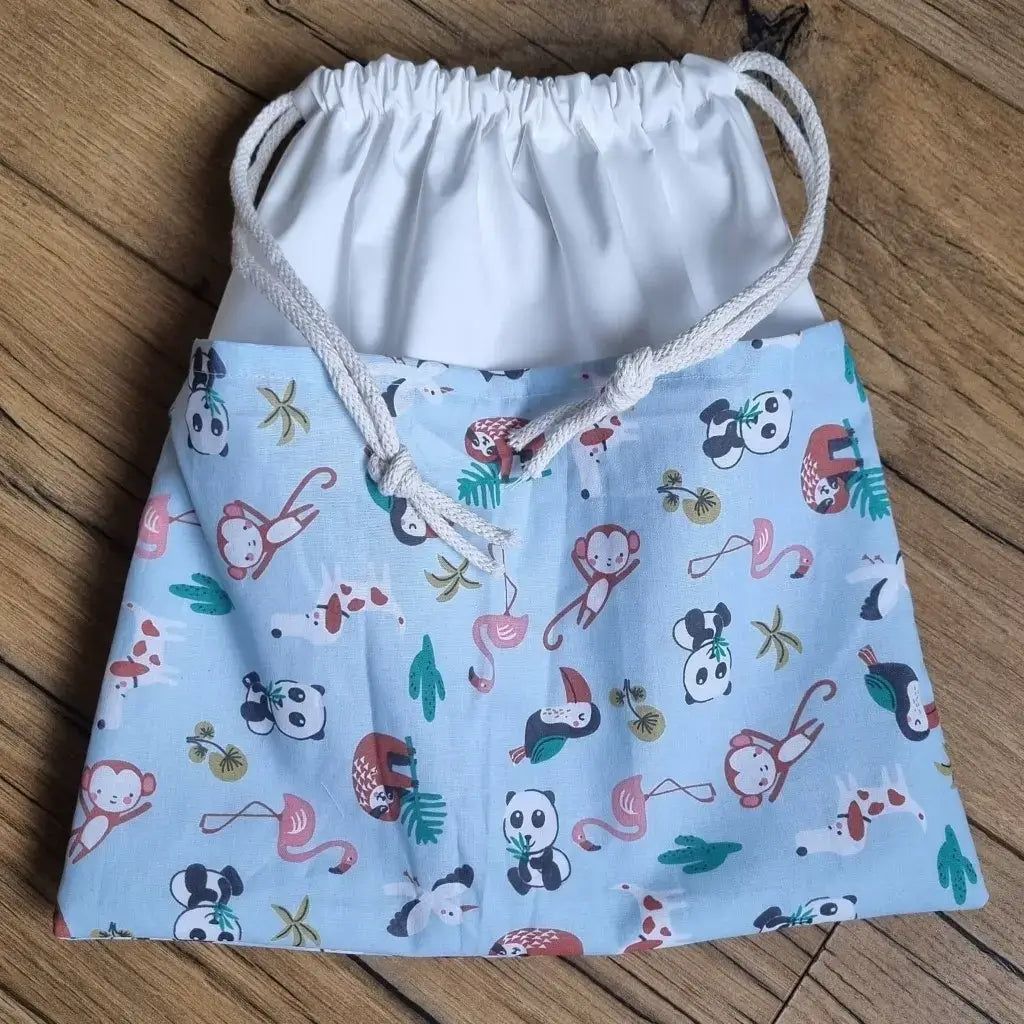 Sac piscine imperméable au format pochon se fermant grâce à deux cordelettes en coton blanc de part et d'autre et cousu avec un tissu imprimé à motif d'animaux de la savane comme des pandas, des toucans, des singes, des flamants roses, ...