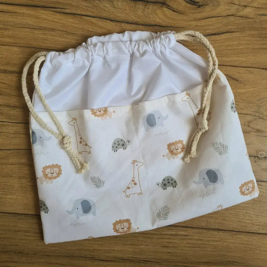 Sac piscine imperméable au format pochon se fermant grâce à deux cordelettes en coton blanc de part et d'autre et cousu avec un tissu imprimé à motif des animaux de la savane comme des éléphants, des girafes, des lions, ...