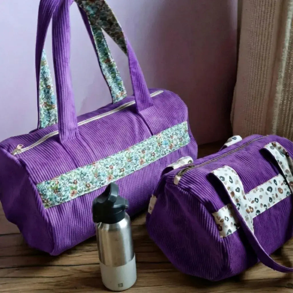 Sacs polochons en velours côtelé violet lavande avec détails fleuris et léopard, posés sur du bois.