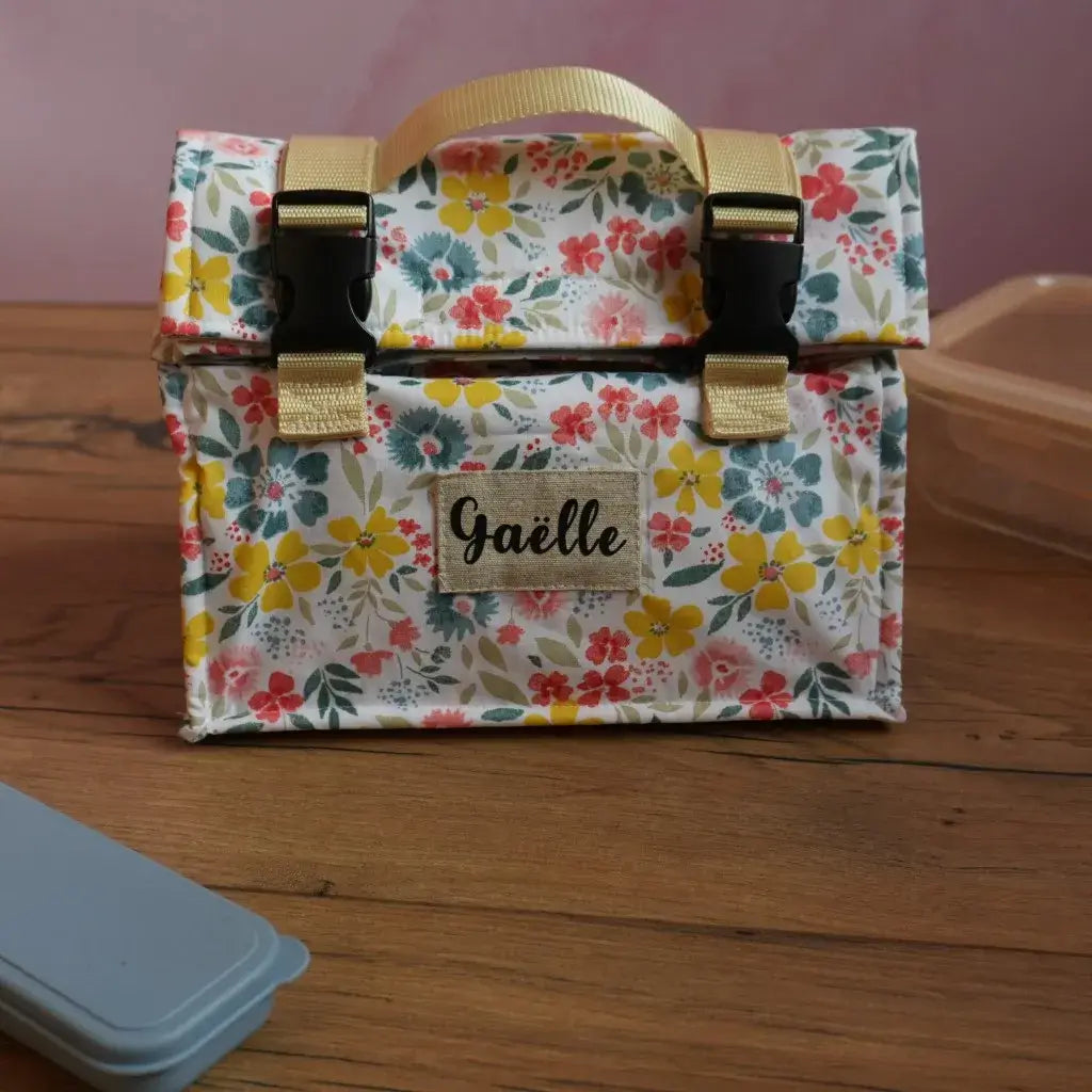 Sac repas isotherme personnalisé en coton enduit à motif fleuri multicolore avec prénom Gaëlle floqué sur une étiquette, équipé de sangles beige et de fermetures à clips noirs, idéal pour transporter déjeuner ou goûter au bureau, à l’école ou en sortie. Lunch bag réutilisable, pratique et fait main.