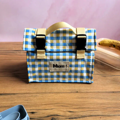 Sac repas isotherme cousu main en coton enduit à carreaux bleus et jaunes, avec poignée en sangle beige, fermetures à clips noirs et étiquette personnalisée “Miam !”, idéal pour transporter déjeuner, goûter ou pique-nique au bureau, à l’école ou en déplacement, alternative zéro déchet aux emballages jetables.