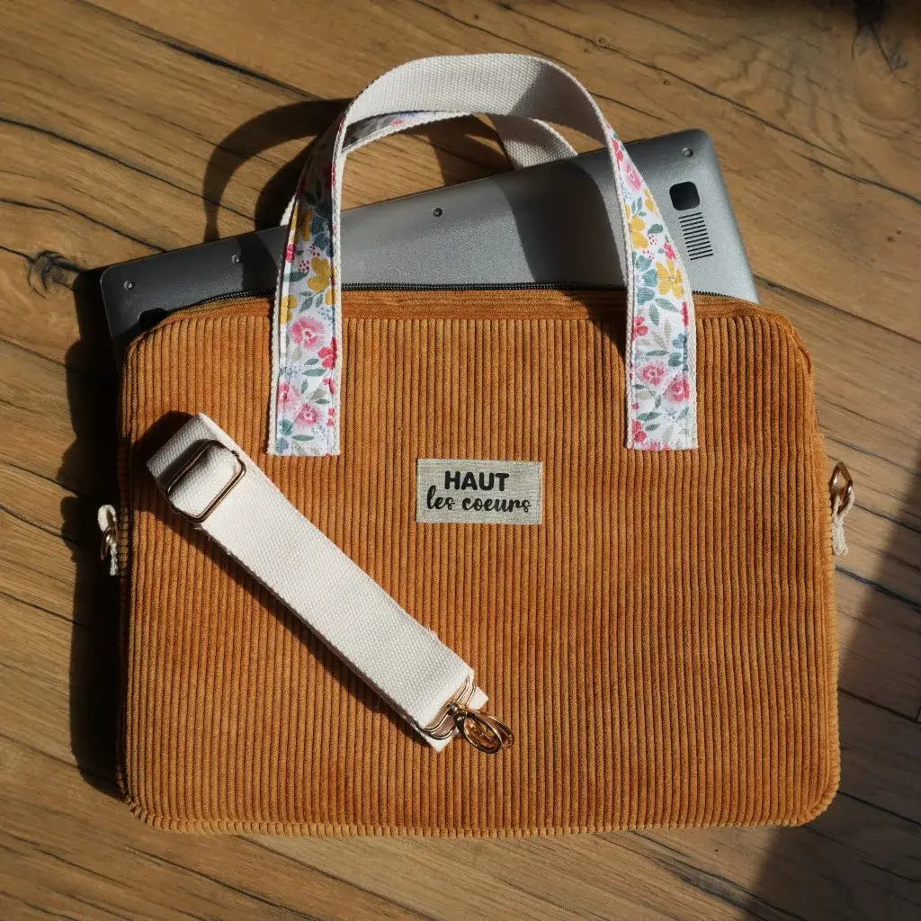 Sacoche pour ordinateur portable en velours côtelé jaune moutarde, avec anses en tissu fleuri et bandoulière réglable en sangle écrue. Le modèle est orné d’une étiquette 'Haut les cœurs' et dispose d’une fermeture éclair pratique. Une sacoche artisanale et tendance, idéale pour transporter son PC ou sa tablette en toute sécurité, alliant style, confort et originalité.
