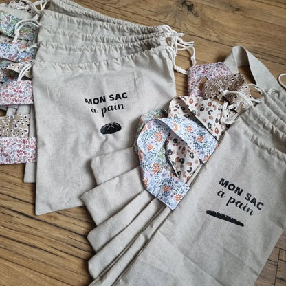 Ensemble de sacs à pain en coton personnalisables et réutilisables. Ceux de gauche sont au format miche de pain. Ceux de droites sont au format baguette. Le motif des anses est différents à chaque fois : il peut être uni, léopard, fleuri ou liberty. Chaque sac comporte une inscription "Mon sac à pain" floquée au centre avec le logo d'une miche de pain ou d'une baguette de pain selon le format du sac.