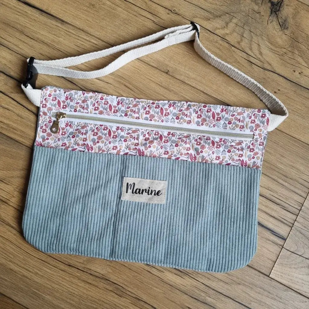 Tablier ceinture en velours côtelé bleu clair personnalisé avec prénom, doté d’une poche zippée en coton imprimé fleuri et d’une ceinture réglable en sangle écrue. Idéal pour couturières, bricoleurs ou créateurs, cet accessoire pratique permet de garder ses outils à portée de main tout en ajoutant une touche unique et élégante, parfait pour allier organisation, confort et style dans ses activités.
