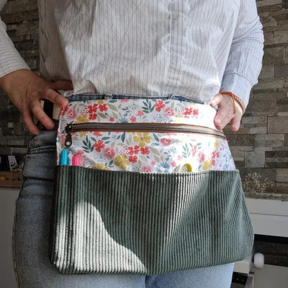 Tablier ceinture porté à la taille, confectionné en velours côtelé vert avec tissu fleuri coloré. Équipé de plusieurs poches, dont une grande poche zippée pour garder ciseaux, stylos et accessoires à portée de main. Idéal pour les activités de couture ou créatives.