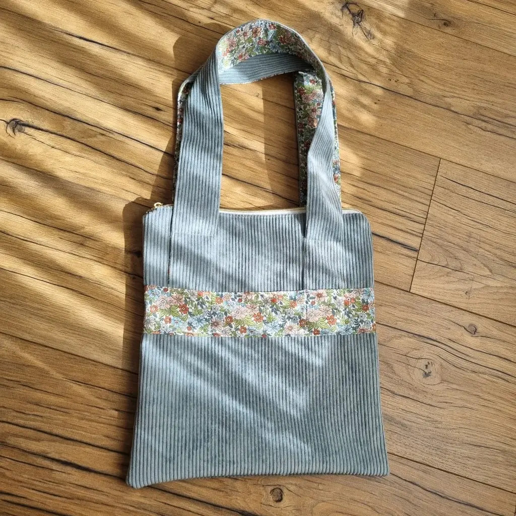 Sac fourre-tout de type tote-bag en velours côtelé de coloris bleu ciel. Le sac présente en façade une bande horizontale en tissu à motif fleuri. Ce même tissu se retrouve également au dos des deux anses.