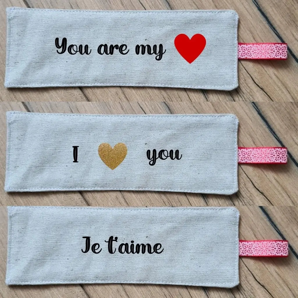 Trois marque-pages en tissu disposés les uns au-dessus des autres. Ces marque-pages en tissu sont personnalisés avec une inscription floquée en noir. Pour celui du haut : "You are my love". Pour celui du milieu : "I love you". Pour celui du bas : "Je t'aime".