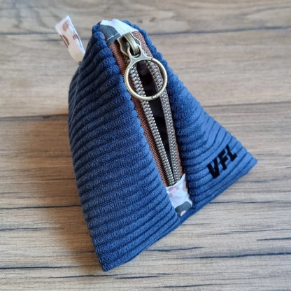 Trousse berlingot en tissu velours côtelé bleu foncé posée sur un parquet en chêne. Ce berlingot est personnalisé avec les initiales "VFL" floquées en noir.