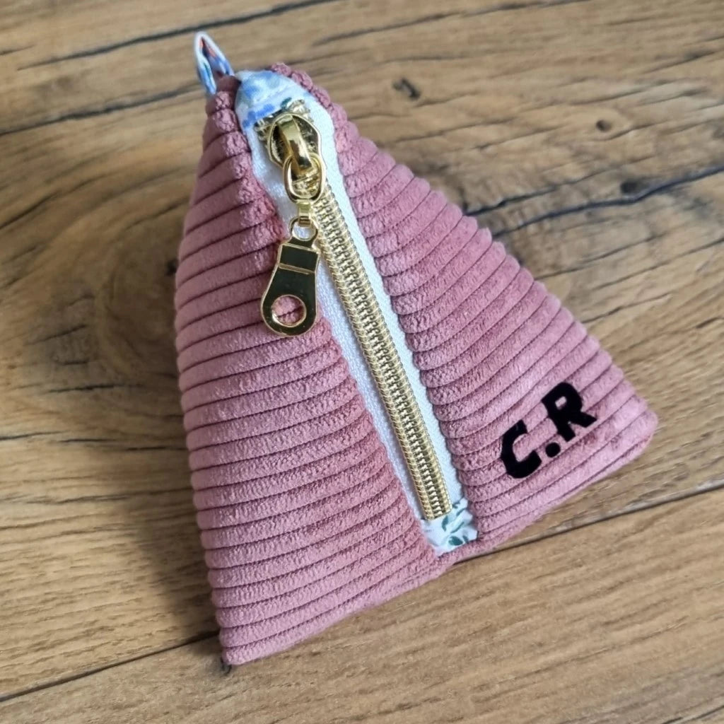 Trousse berlingot en tissu velours côtelé rose posée sur un parquet en chêne. Cette trousse est personnalisée avec les initiales "C.R." floquées en noir.